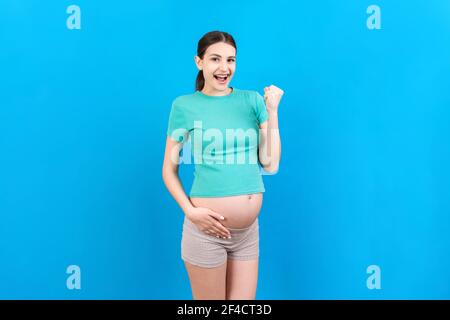 Young beautiful pregnant woman on isolated colored background celebrating surprised and amazed for success with arms raised and open eyes. Winner conc Stock Photo