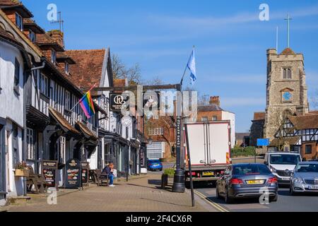 Pinner Village High Street. Historic Queen’s Head Pub, & Pizza Express on the left & Saint John the Baptist, Medieval hilltop church in background. Stock Photo