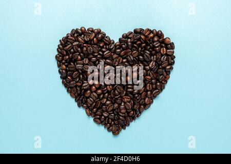 Coffee beans in shape of heart on blue background. Creative minimal coffee drink concept. Stock Photo
