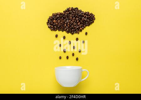 Coffee beans in shape of rainy cloud with white cup on yellow background. Creative minimal coffee drink concept. Stock Photo