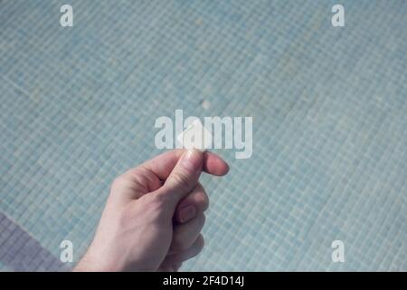 Close-up of white tile holding by a hand on the empty stoneware pool with a little hole in the background. Empty pool. Stock Photo