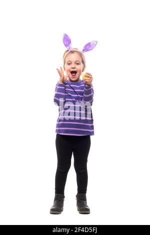 Joyful excited young girl with bunny ears and Easter egg screaming at camera. Full body isolated on white background Stock Photo