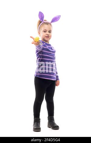 Caring young cute girl with bunny ears sharing and giving Easter egg at camera. Full body isolated on white background Stock Photo
