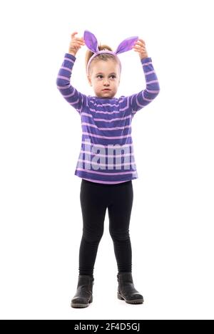 Adorable girl child looking away touching Easter bunny hat ears with uncertainty. Full body isolated on white background Stock Photo