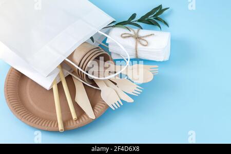 Paper bag full of eco friendly disposable tableware on light blue background Stock Photo