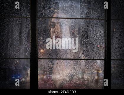 Thoughtful young woman looking through a rainy window Stock Photo