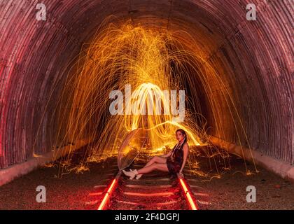 Beautiful woman sitting on railway tracks surrounded by spinning wire wool Stock Photo
