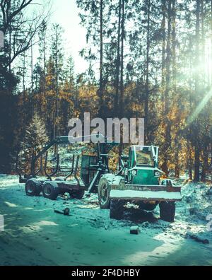 Old tractor with a trailer against forest in winter, covered with the snow Stock Photo