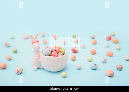 Easter bunny figurine with mini candies and scattered candies around it on a blue background Stock Photo