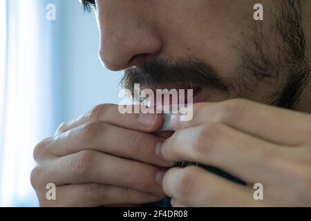 Teenage man making rolls-up cigarette sealing a paper by licking it with tongue. makes Rolling Tobacco Cigarette. Portrait of young man licking edge o Stock Photo