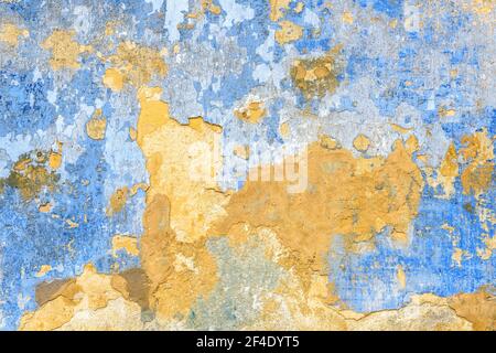 Old wall texture background, broken plaster for backdrop or wallpaper. Rough peeling stone wall surface painted in yellow and blue colors. Cracked gru Stock Photo