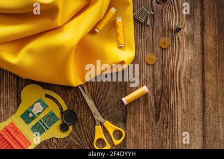 Sewing accessories and yellow fabric on wooden table. Sewing threads, needles, pins, buttons and scissors. Top view, flat lay concept. Accessories Stock Photo