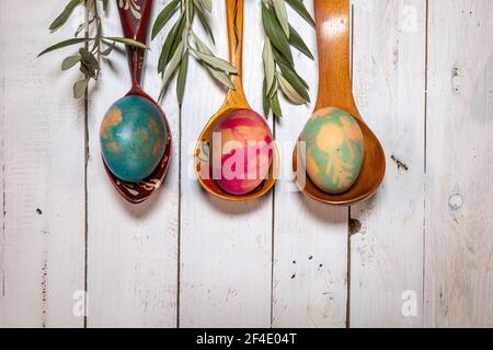Flatlay Easter composition. Wooden spoons with coloured eggs and olive branches on a shabby chic background. Stock Photo