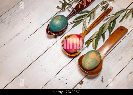 Flatlay Easter composition. Wooden spoons with coloured eggs and olive branches on a shabby chic background. Stock Photo