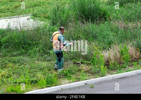 Process of lawn trimming with hand mower.lawn mower worker cutting grass in green field.Worker mowing tall grass with petrol lawn trimmer in city park Stock Photo