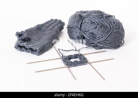 Still life of knitting on knitting needles, ball of wool, ready-made mitten isolated on white background Stock Photo
