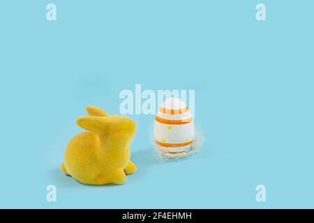 Yellow Easter bunny rabbit with painted egg on blue background. Easter holiday concept. minimalism Stock Photo