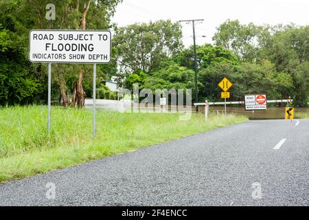 Warning sign that road is subject to flooding and a barrier and road closed sign due to flooding and water in tropical North Queensland. Stock Photo