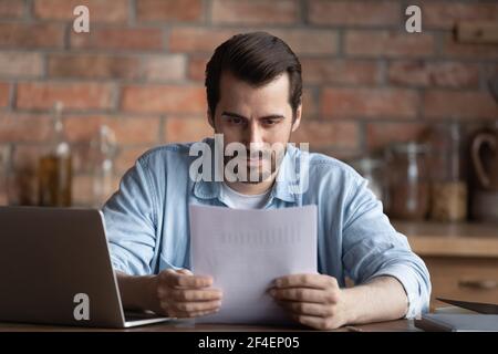 Serious man work on computer reading paperwork Stock Photo