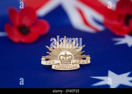 An Australian army rising sun badge on an Australian flag with red poppies in the background for Anzac Day or Remembrance Day.  Selective focus. Stock Photo