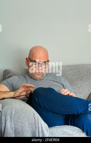 Bald headed middle-ages man sitting on sofa and looking down as he uses his iPad Stock Photo