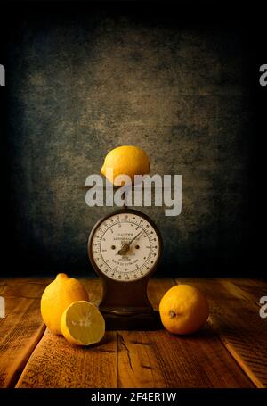 Several fresh Lemons and an old weighing scales placed on a rustic oak table Stock Photo