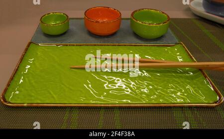 Kitchen accessories, lively green ceramic sushi set consisting of a rectangular plate, bowls and wooden chopsticks. Stock Photo