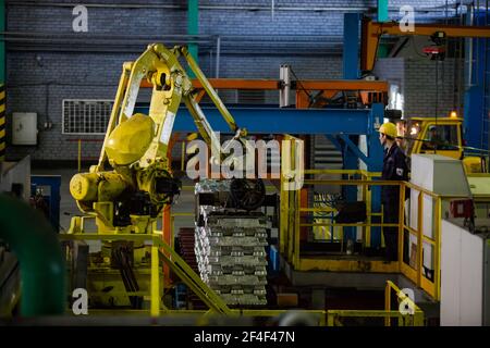 Pavlodar Aluminium electrolysis plant. Aluminium ingots packing machine. Young asian operator worker in yellow hardhat. Stock Photo