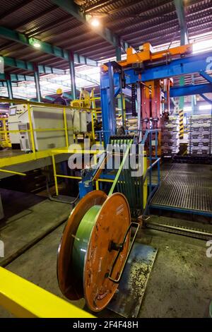 Pavlodar Aluminium electrolysis plant. Aluminium ingots packing machine. Young asian operator worker in yellow work helmet. Stock Photo