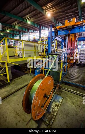 Pavlodar Aluminium electrolysis plant. Aluminium ingots packing machine. Young asian operator worker in yellow work helmet. Stock Photo