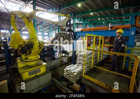 Pavlodar Aluminium electrolysis plant. Aluminium ingots packing machine. Young asian operator worker in yellow hardhat. Stock Photo