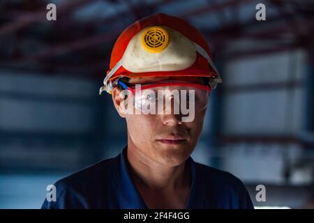 Taldykorgan, Kazakhstan-June 06 2012: Accumulator recycling plant. Portrait of young Asian worker in orange hardhat, protective glass and respirator. Stock Photo