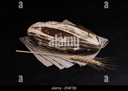 Artisan sourdough rye bread on dark background. Whole loaf of bread on textile napkin and rye spikelet Stock Photo
