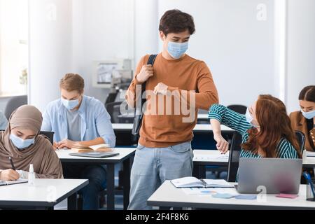 Diverse students wearing face masks greeting and bumping elbows Stock Photo
