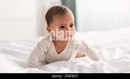 Portrait of sad black baby crying and crawling on bed Stock Photo