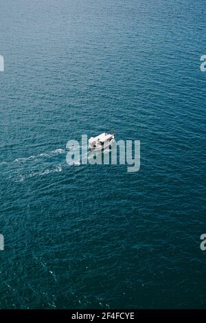 Small tourist boat floats on water texture, aerial frame from helicopter. Stock Photo