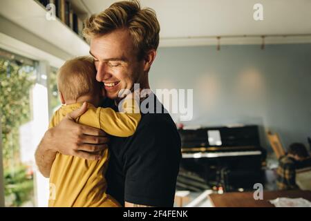 Man on paternity leave taking care of his new born baby boy. Man carrying his son in his arms at home. Stock Photo