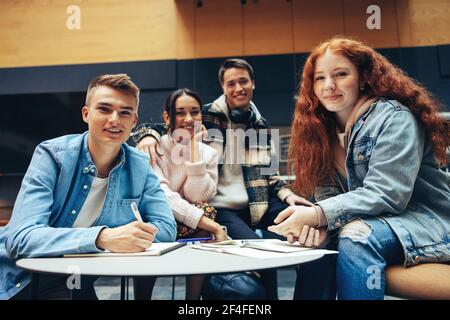 Students doing group studies in high school and looking at camera. Young men and women sitting in library working on project. Stock Photo