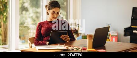Woman artist sitting at table and using graphic tablet for making illustrations. Female illustrator working from home. Stock Photo