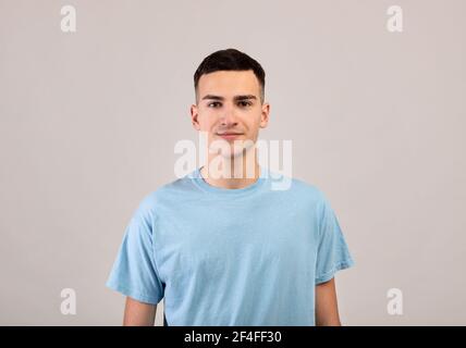 Portrait of positive young guy in t-shirt looking at camera on light grey studio background Stock Photo