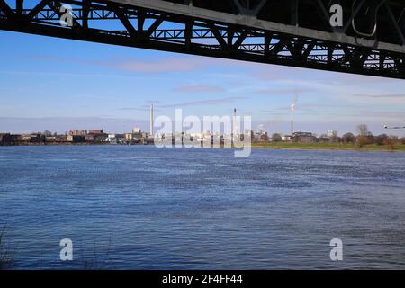 Krefeld (Uerdingen) - March 1. 2021:  View beyond steel bridge over river rhine on  industrial area with factories and chimneys against blue sky Stock Photo