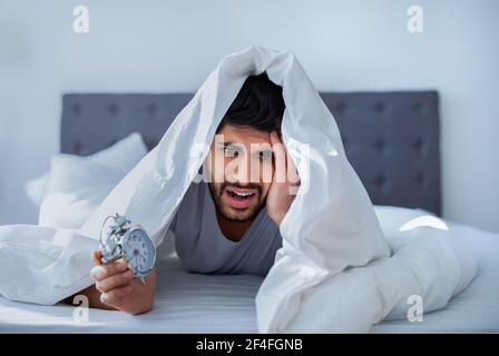 Arab man suffering from pain, lying in bed under blanket, waking up in the morning Stock Photo