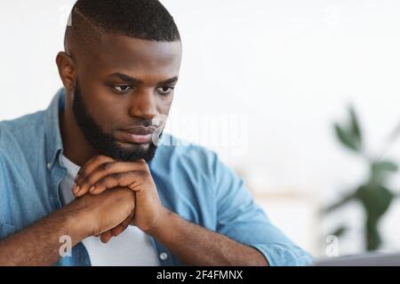 Deep in thoughts. Pensive millennial African American man leaning head on hands Stock Photo