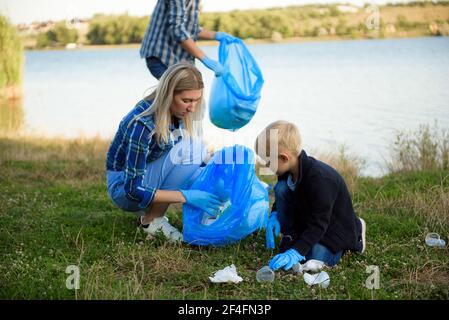 volunteering, charity, people and ecology concept, volunteers using garbage bag while collecting litter Stock Photo