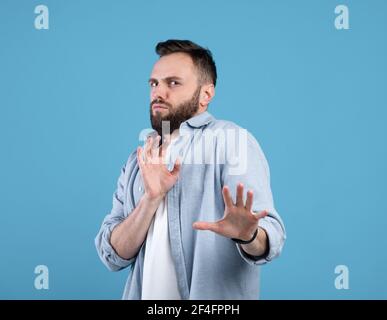 Repulsed millennial guy rejecting something, making STOP gesture over blue studio background Stock Photo
