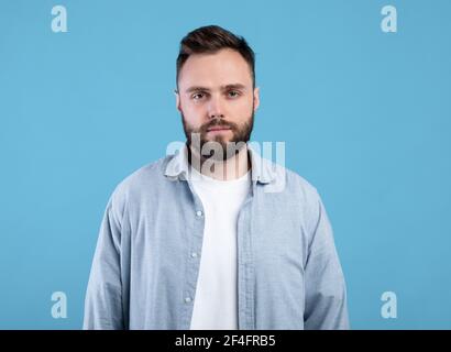Portrait of serious young guy looking at camera on blue studio background Stock Photo
