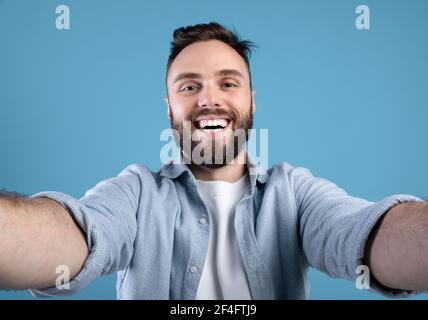 Joyful bearded guy taking selfie on blue studio background Stock Photo