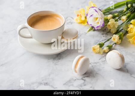 Macaroons with white cup of coffee, bright beautiful flowers on marble background.Beautiful breakfast for woman. Spring concept.Copy space Stock Photo