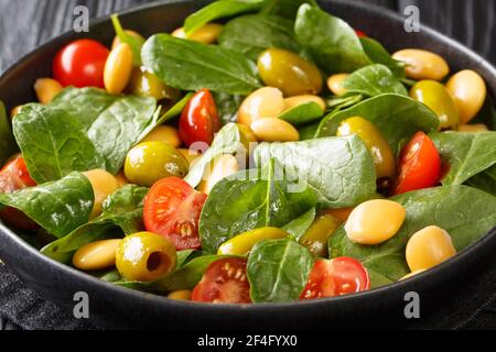 Mediterranean vegan salad of spinach, lupine beans, tomatoes and olives close-up in a plate on the table. horizontal Stock Photo