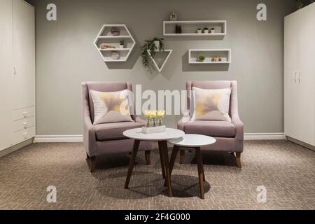 Grey cloth upholstered armchairs and white round tables and storage cabinets in den in basement of contemporary home Stock Photo